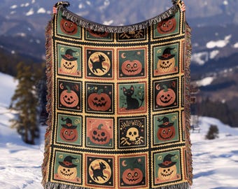 May include: A Halloween-themed throw blanket with a repeating pattern of jack-o'-lanterns, black cats, and a skull. The blanket has a black fringe and is held up against a snowy mountain backdrop.