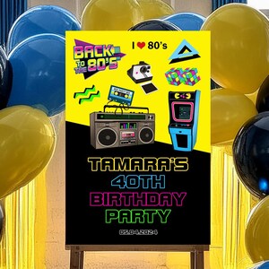 May include: A black chalkboard sign with a yellow and neon pink graphic design featuring a boombox, cassette tape, and a video game. The text on the sign reads "Back to the 80's", "I &hearts; 80's", "Tamara's 40th Birthday Party", and "09.04.2024". The sign is surrounded by yellow, blue, and black balloons.