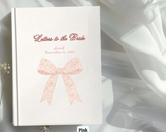 May include: A white book titled "Letters to the Bride" with the name "Sarah" and the date "November 26, 2025" in a script font. A pink floral bow illustration is centered on the cover. The word "Pink" is at the bottom.
