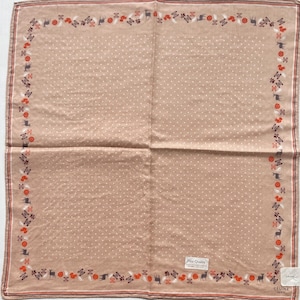 Op de afbeelding: Een vierkante sjaal in beige met een wit stippenpatroon. De rand heeft een decoratief patroon met herten, bloemen en andere elementen in rood, grijs en wit. De sjaal heeft een "Fine Quality" label en de merknaam "CELINE PARIS".