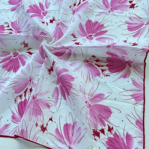 Op de afbeelding: Witte zakdoek met een herhalend patroon van roze bloemmotieven. De bloemen hebben een aquareleffect met dunne, donkerroze omtrekken. De randen zijn afgewerkt met een dunne, donkerrode rand. Het Christian Dior-logo is zichtbaar.