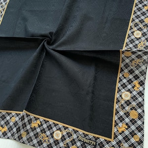 Peut inclure: Foulard carré noir avec un centre texturé et une bordure à motifs. La bordure présente un motif à carreaux noir et blanc avec des accents dorés, notamment des pièces de monnaie, des figurines de chien et la marque "Burberrys".
