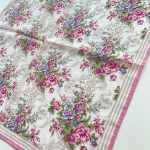 Könnte beinhalten: Ein quadratisches Tuch mit einem Blumenmuster aus rosa und blauen Blumen auf cremefarbenem Hintergrund. Der Schal hat einen rosa Rand mit beigen Streifen und das Burberrys-Logo.