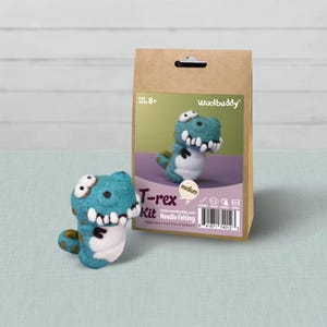 May include: A Woolbuddy T-rex needle felting kit in a brown paper bag with a teal and white felt dinosaur figure. The packaging features the text T-rex Kit, Needle Felting, and states it makes one T-rex 3 to 4 inches tall for ages 8 and up.