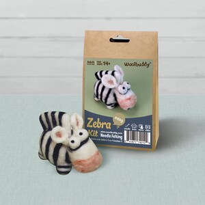 May include: A Woolbuddy needle felting kit in a brown paper bag featuring a black and white striped zebra illustration. The kit includes materials to create a 3 to 4 inch zebra. A finished felted zebra figure with black stripes and a pinkish snout sits in front.