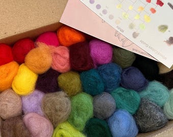 May include: A cardboard box filled with numerous small, round balls of colourful wool roving in shades of red, orange, yellow, green, blue, purple, pink, brown, grey, and black, accompanied by a printed card labelled Mixed Colors Guide.