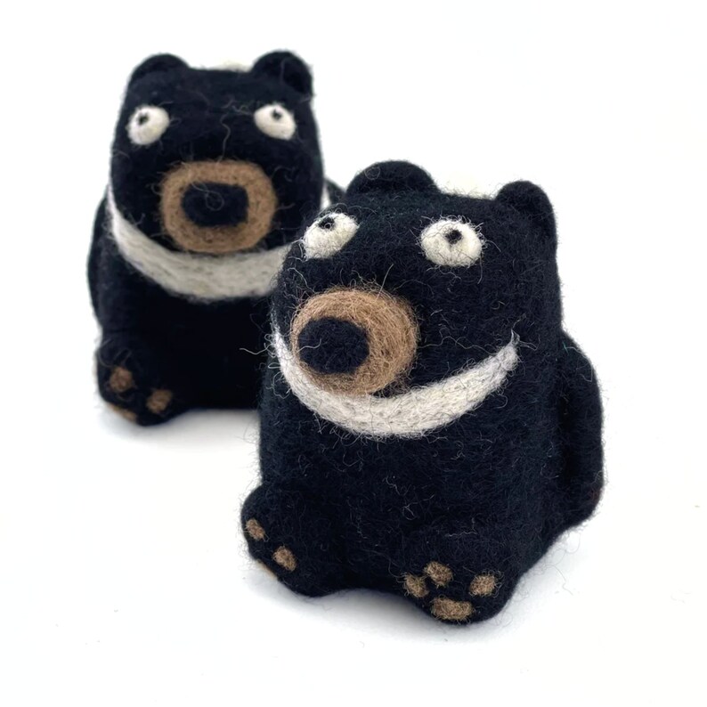 Puede incluir: Dos figuritas de animales de fieltro negro con detalles blancos. Las figuritas tienen narices de fieltro marr&oacute;n y grandes ojos blancos. Las figuritas est&aacute;n sentadas sobre una superficie blanca.