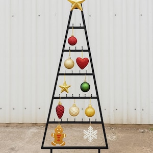 以下が含まれることがあります： さまざまなオーナメントが付いた、黒い金属製のクリスマスツリー型のディスプレイスタンド。オーナメントには、赤、金、緑のボール、金の星、赤いハート、ジンジャーブレッドマン、雪の結晶が含まれています。