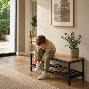 Puede incluir: Un banco de entrada rectangular con una superficie superior de madera clara y un marco de metal negro con un estante inferior de listones para guardar zapatos. El banco está colocado contra una pared y tiene una planta verde en maceta.