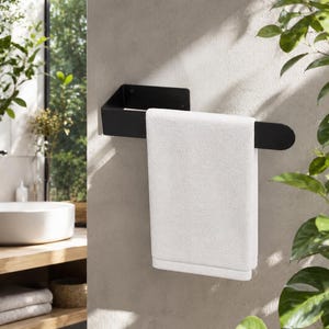 May include: A matte black metal towel rail mounted to a wall, featuring a rectangular base plate and a horizontal arm with a rounded end. A single, folded white rectangular towel hangs over the rail, draping down in a smooth, vertical orientation.