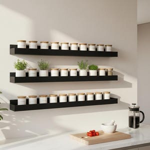 May include: Three black floating shelves on a white wall, each holding small white jars with wooden lids. Some shelves also display small potted herbs. A kitchen setting with a plant in a terracotta pot.