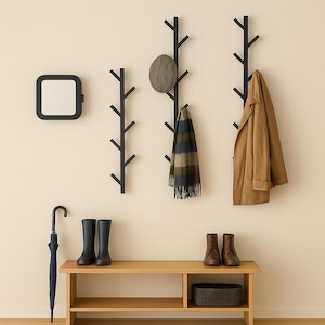 May include: A modern entryway setup featuring black tree-shaped coat racks, a square mirror, a wooden bench, and various accessories. A tan coat, a gray hat, and a patterned scarf hang on the racks. Boots, shoes, and an umbrella complete the scene.