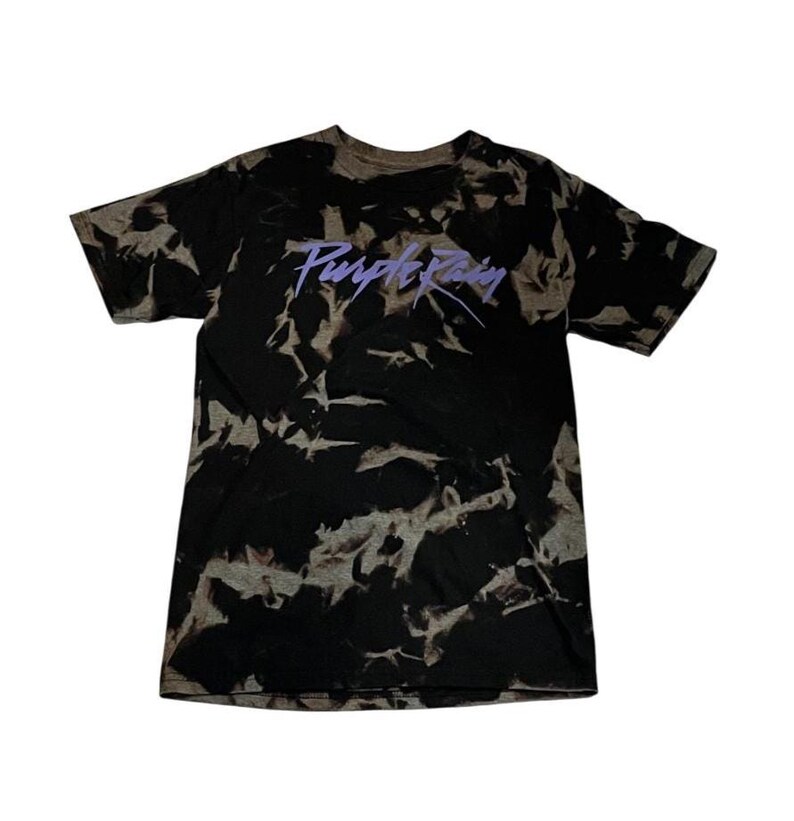 May include: A black and white tie-dye t-shirt with a purple "Purple Rain" logo printed on the front.
