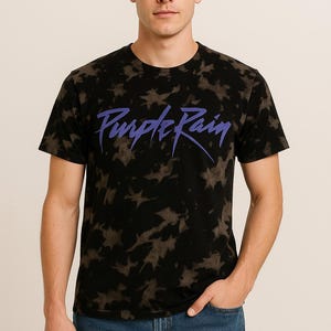 May include: A black t-shirt with a tie-dye pattern and the words "Purple Rain" in purple lettering.