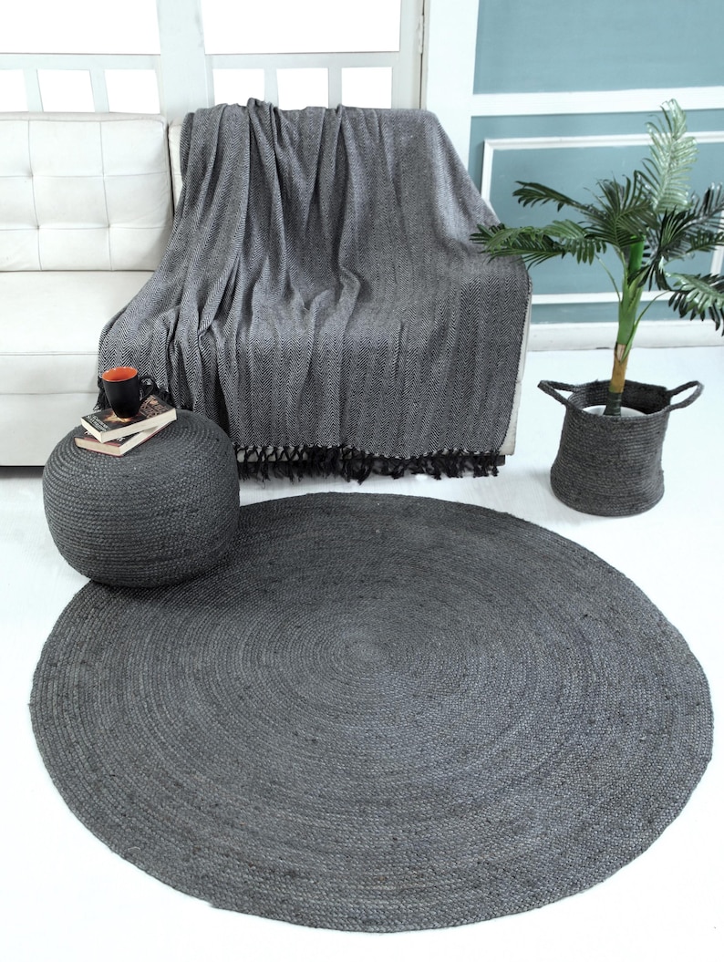 May include: A round, dark gray jute rug with a woven texture. The rug is placed on a white floor in a living room setting.