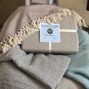 Puede incluir: Tres mantas de algodón de tejido de gofre en beige, gris y azul claro. La manta beige está doblada y tiene una etiqueta que dice "Honeycomb 100% Cotton Throw".