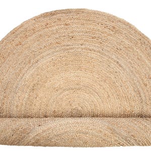 May include: A natural fiber, round, jute rug with a half-circle shape. The rug is made of woven jute and has a natural, earthy color.