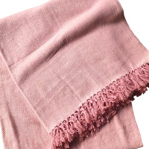 Pode incluir: Uma manta de arremesso macia de cor rosa com um padr&atilde;o de espinha de peixe e guarni&ccedil;&atilde;o de franjas.