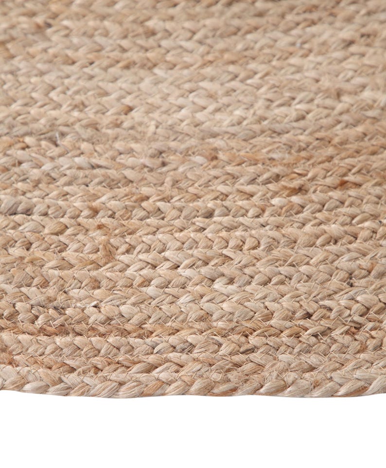 May include: A close-up of a natural fiber rug made from jute. The rug has a woven texture and a light brown color.