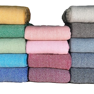 May include: A stack of 12 woven blankets in various colours, including yellow, green, blue, pink, and grey. The blankets have a herringbone pattern and are folded neatly.
