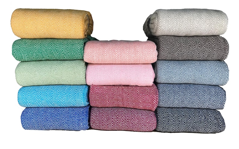 Pode incluir: Uma pilha de 12 cobertores tecidos em v&aacute;rias cores, incluindo amarelo, verde, azul, rosa e cinza. Os cobertores t&ecirc;m um padr&atilde;o de espinha de peixe e est&atilde;o dobrados cuidadosamente.
