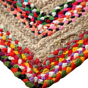 May include: Close-up of a handmade jute rug with a colorful, woven border. The rug features a natural beige center with a chevron design, and a vibrant border of red, green, orange, and purple fabric.