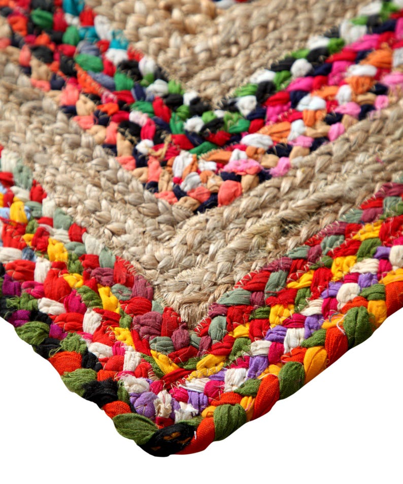 May include: Close-up of a handmade jute rug with a colorful, woven border. The rug features a natural beige center with a chevron design, and a vibrant border of red, green, orange, and purple fabric.