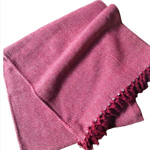Pode incluir: Uma manta de arremesso chevron rosa e branco com uma borda de franja.