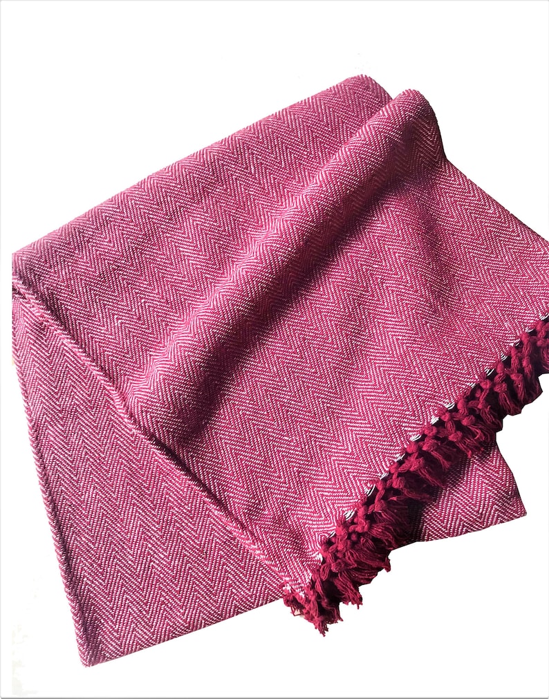 Pode incluir: Uma manta de arremesso chevron rosa e branco com uma borda de franja.