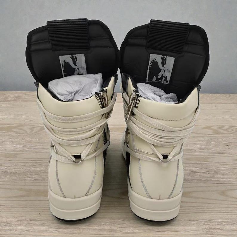 Pode incluir: Par de t&ecirc;nis de cano alto creme e preto. Os t&ecirc;nis apresentam fecho de z&iacute;per, cadar&ccedil;os enrolados e uma l&iacute;ngua preta acolchoada. O design inclui um logotipo na l&iacute;ngua e uma sola grossa.