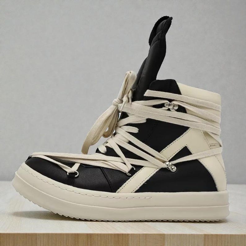 Pode incluir: T&ecirc;nis de cano alto em preto e branco sujo. O cal&ccedil;ado apresenta um design exclusivo com cadar&ccedil;os envolventes e uma l&iacute;ngua alta e acolchoada. A sola &eacute; branca suja e o t&ecirc;nis tem ilh&oacute;s de metal.