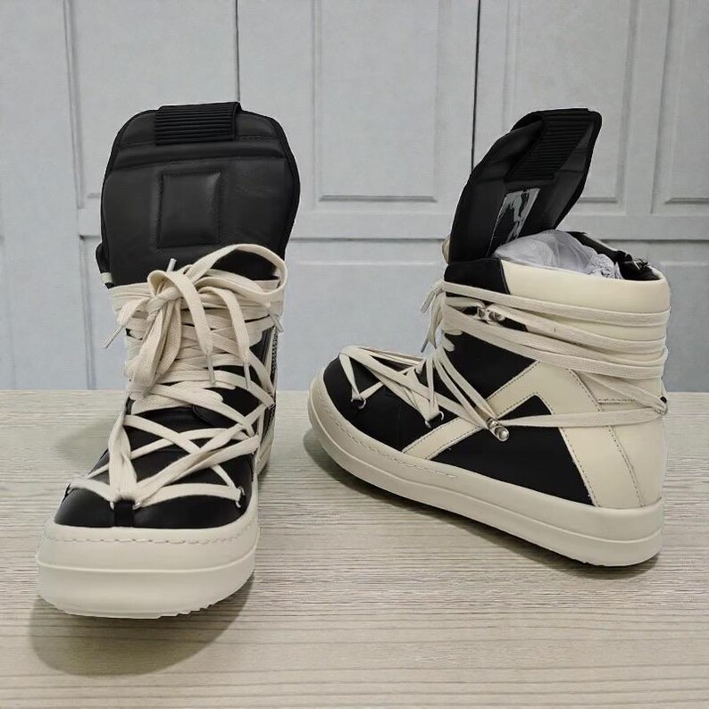 Pode incluir: Par de t&ecirc;nis de cano alto em preto e branco sujo. Os t&ecirc;nis apresentam um design exclusivo com cadar&ccedil;os creme cruzados e uma sola grossa branco sujo. A l&iacute;ngua &eacute; preta e a parte superior &eacute; uma mistura de pain&eacute;is pretos e branco sujo.