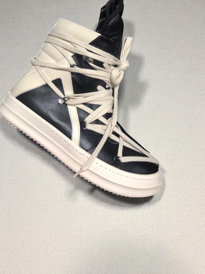 Pode incluir: T&ecirc;nis de cano alto em preto e creme. O t&ecirc;nis apresenta um design em camadas com uma sola grossa esbranqui&ccedil;ada e cadar&ccedil;os creme intrincados. A parte superior &eacute; uma combina&ccedil;&atilde;o de pain&eacute;is pretos e creme. A l&iacute;ngua &eacute; preta.