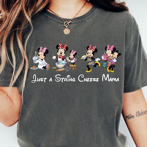 May include: Dark gray t-shirt featuring a graphic of Minnie Mouse characters in various poses, with the text "Just a String Cheese Mama" in white script. The shirt is a casual, comfortable style.