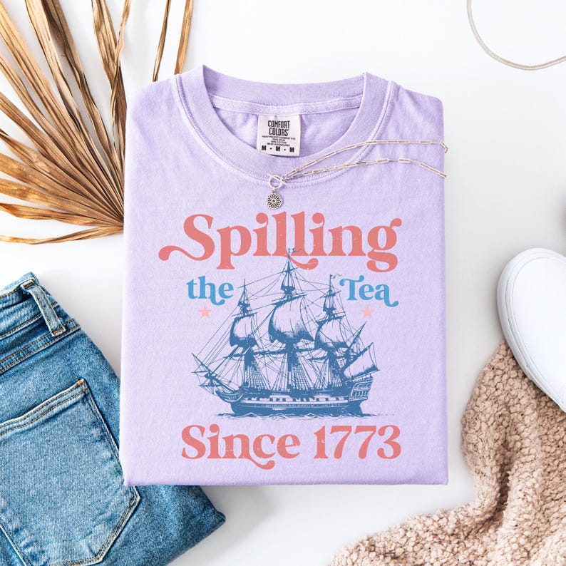 May include: Purple t-shirt with a vintage-style graphic of a ship and the text "Spilling the Tea Since 1773".