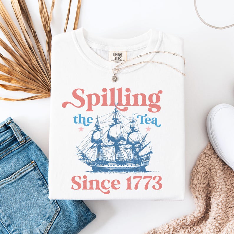 May include: White t-shirt with a blue and red graphic of a ship and the text "Spilling the Tea Since 1773".