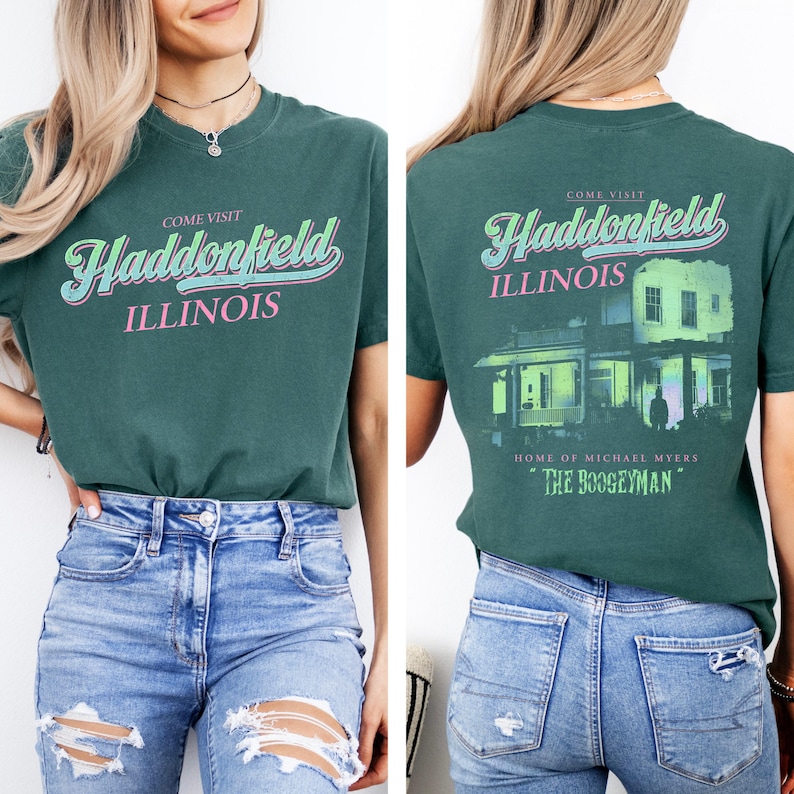 May include: Teal green t-shirt with the text "COME VISIT HADDONFIELD ILLINOIS" in a retro font. The back of the shirt features a house graphic with the text "HOME OF MICHAEL MYERS" and "THE BOOGEYMAN".