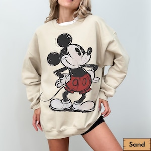 Puede incluir: Sudadera color arena con un gr&aacute;fico desgastado de Mickey Mouse en negro, rojo y blanco. El personaje de dibujos animados est&aacute; en una pose cl&aacute;sica. La sudadera tiene mangas largas y cuello redondo.