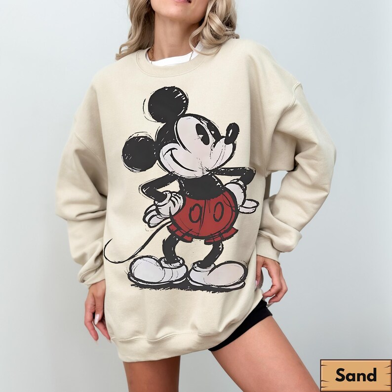 Puede incluir: Sudadera color arena con un gr&aacute;fico desgastado de Mickey Mouse en negro, rojo y blanco. El personaje de dibujos animados est&aacute; en una pose cl&aacute;sica. La sudadera tiene mangas largas y cuello redondo.