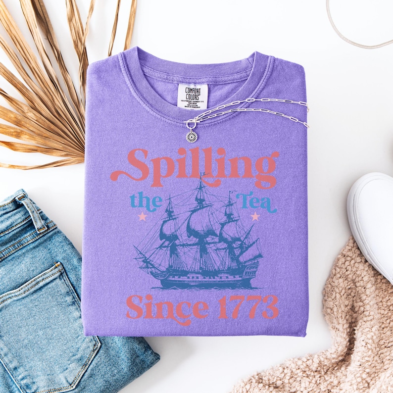 May include: Purple t-shirt with a vintage-style graphic of a ship and the text "Spilling the Tea Since 1773".