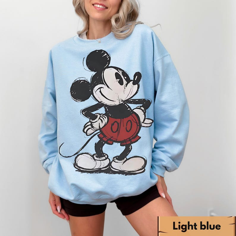 Puede incluir: Sudadera azul claro con un gr&aacute;fico desgastado de Mickey Mouse en negro, rojo y blanco. La sudadera tiene cuello redondo y mangas largas. El texto "Light blue" est&aacute; en la parte inferior de la imagen.