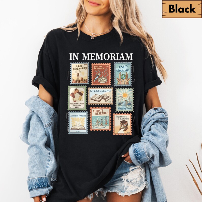 May include: Black t-shirt with the words "IN MEMORIAM" above a grid of nine postage stamp designs. Each stamp features a different graphic and text, including "Public Broadcasting," "Vaccine Research," and "USAID Global Aid."