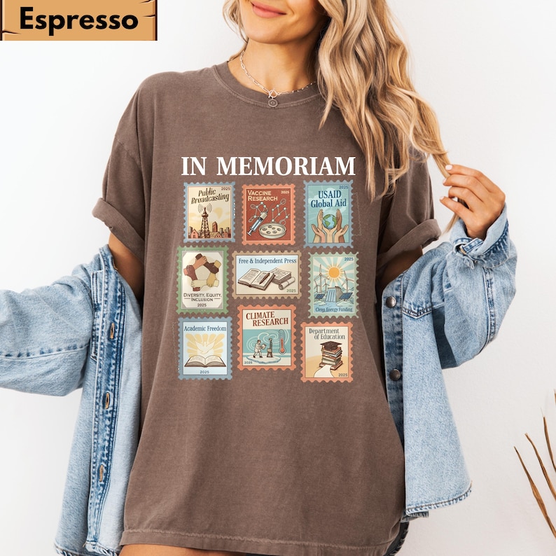 May include: Espresso-colored t-shirt with the words "IN MEMORIAM" above a collection of postage stamp-style graphics. The stamps depict various themes, including "Public Broadcasting," "Vaccine Research," and "USAID Global Aid."