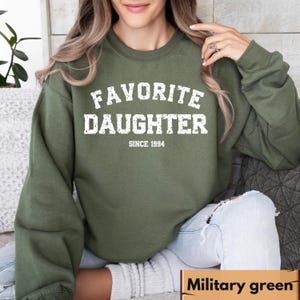 Puede incluir: Sudadera verde militar con el texto blanco "FAVORITE DAUGHTER SINCE 1994". La sudadera de cuello redondo est&aacute; hecha de un material suave. La esquina inferior derecha de la imagen tiene el texto "Military green".