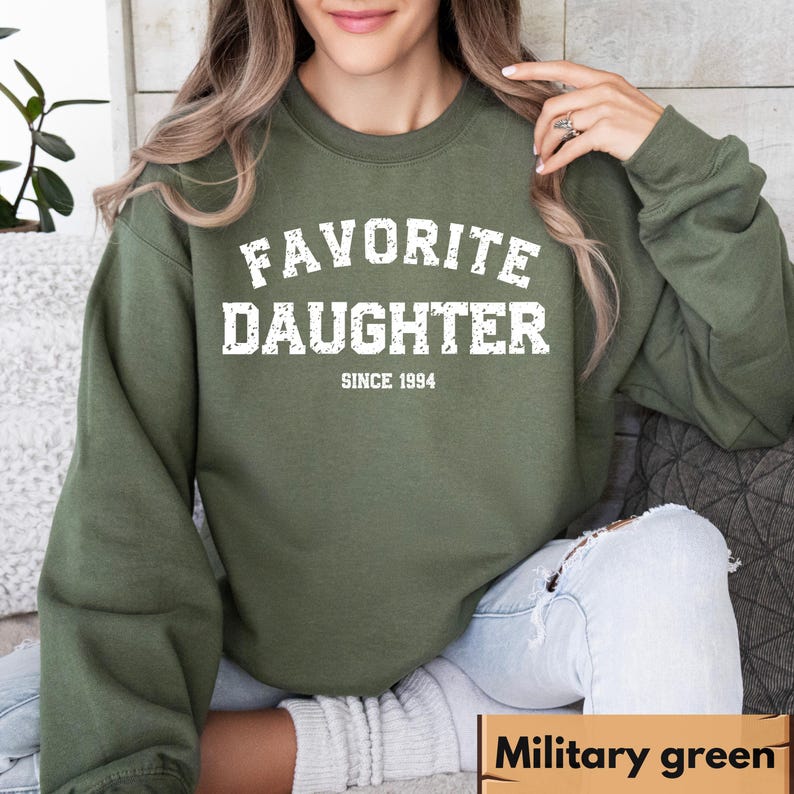 Puede incluir: Sudadera verde militar con el texto blanco "FAVORITE DAUGHTER SINCE 1994". La sudadera de cuello redondo est&aacute; hecha de un material suave. La esquina inferior derecha de la imagen tiene el texto "Military green".