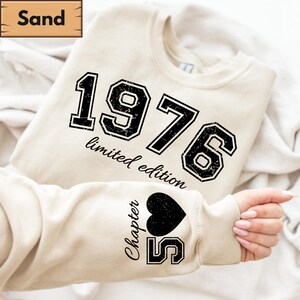 Può includere: Felpa color sabbia con l'anno "1976" e le parole "limited edition" stampate in nero. La manica presenta un cuore nero e il testo "Chapter 55".