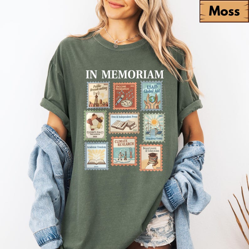 May include: A moss green t-shirt with the words "IN MEMORIAM" above a collection of postage stamp-style graphics. The stamps depict various themes, including "Public Broadcasting," "Vaccine Research," and "Climate Research."