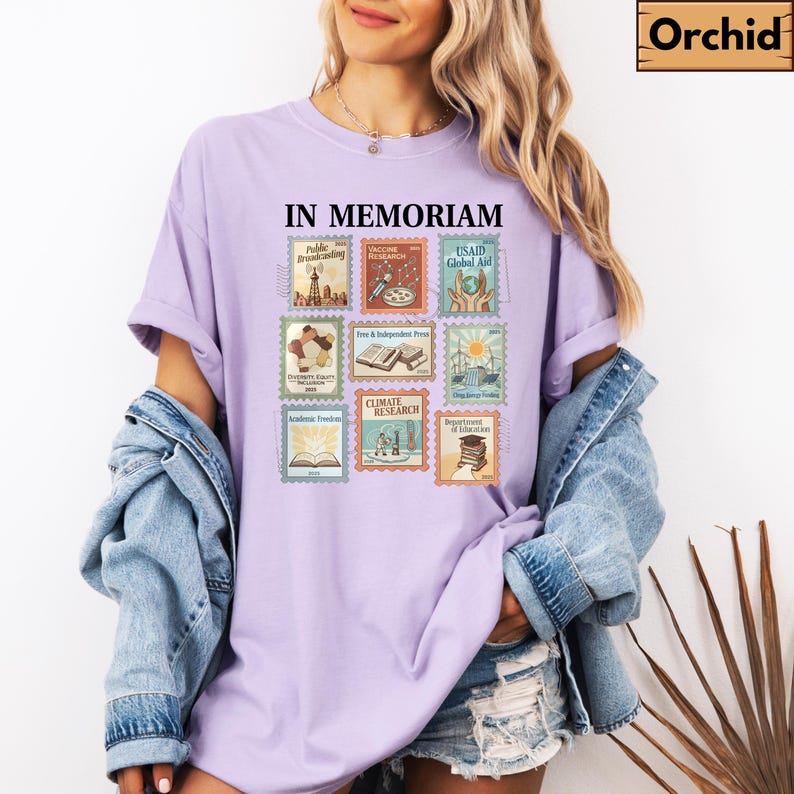 May include: A light purple t-shirt with the words "IN MEMORIAM" above nine postage stamp designs. The stamps feature illustrations related to public broadcasting, vaccine research, and climate research.