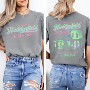 May include: Gray t-shirt with the words "Come Visit Haddonfield Illinois" in a retro font on the front. The back of the shirt features a green and blue graphic of a house with the text "Home of Michael Myers The Boogeyman."