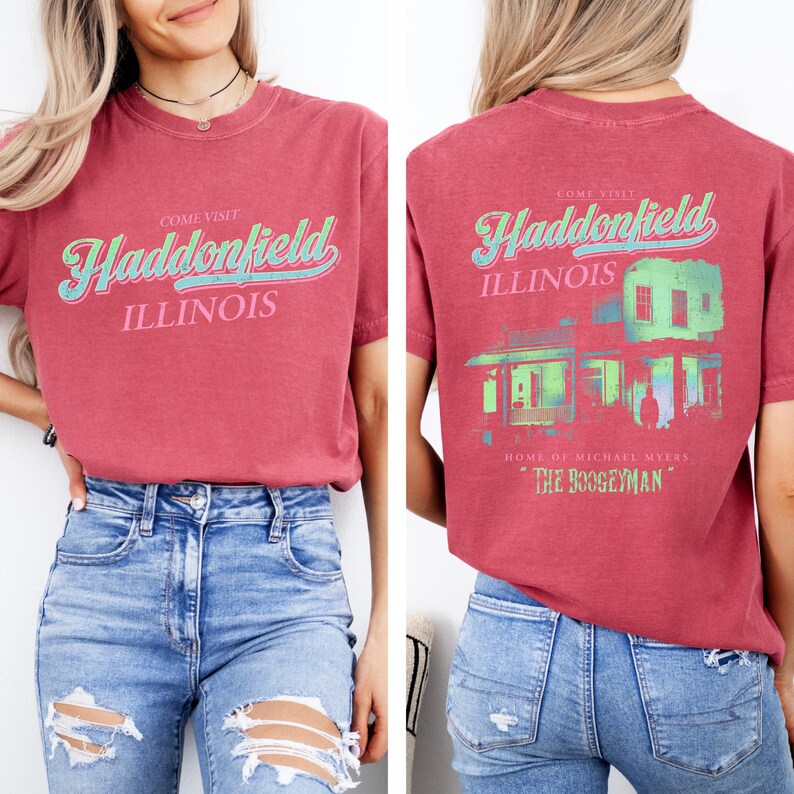 May include: A red t-shirt with the words "Come Visit Haddonfield Illinois" in a retro font. The back of the shirt features a graphic of a house and the text "Home of Michael Myers, The Boogeyman."